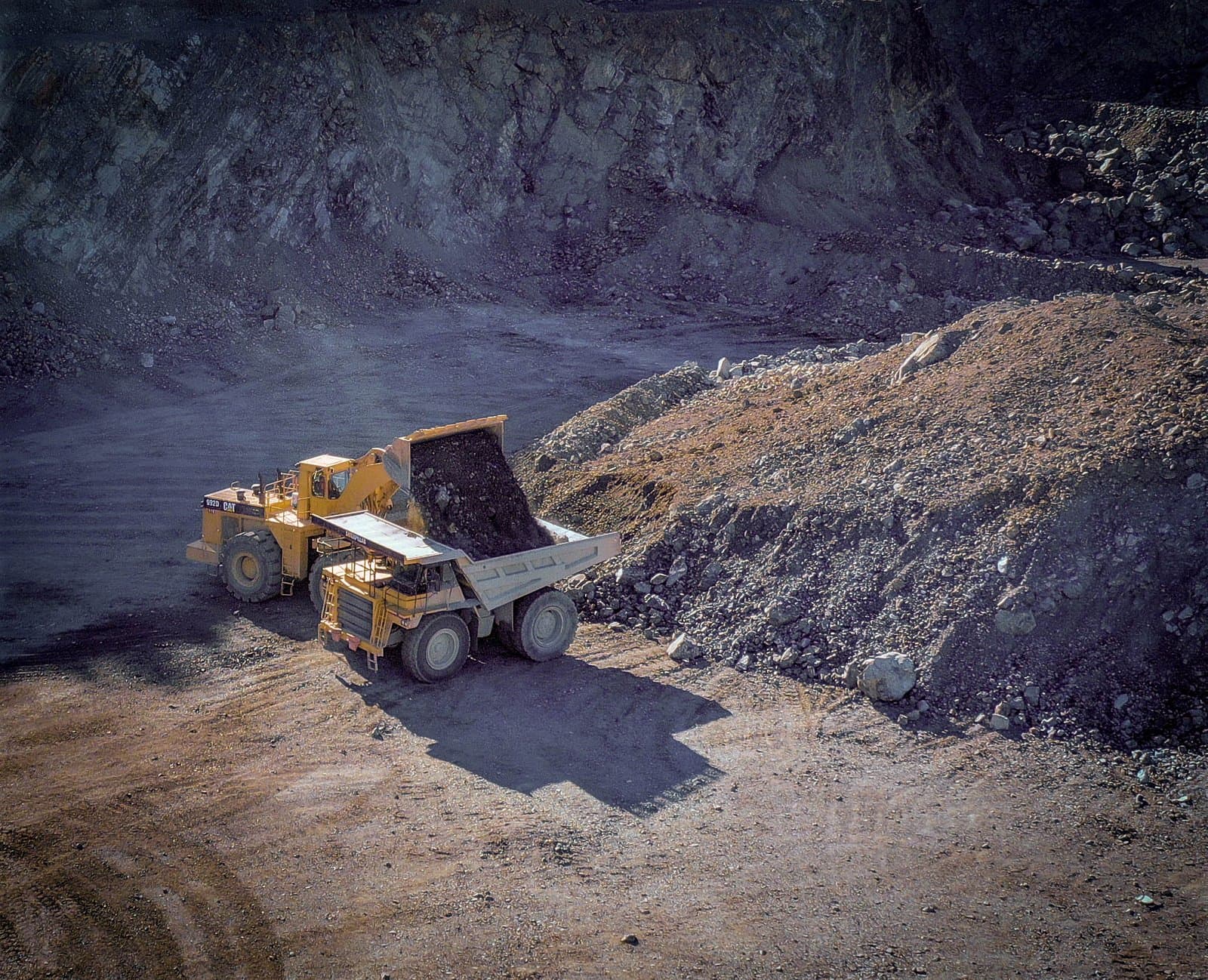 A large front-end loader filling a haul truck with crushed aggregate.